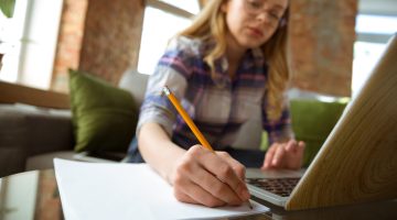 Young woman studying at home during online courses or free information by herself. Becomes musician, violinist while isolated, quarantine against coronavirus spreading. Using laptop, smartphone, headphones.